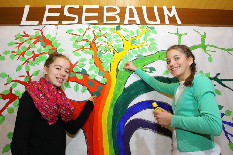 Maria Osl und Isabella Kopf aus der 2b kleben dem Lesebaum neue Blätter an. Jedes Blatt steht für ein gelesenes Buch. Fotos: VN/Hofmeister