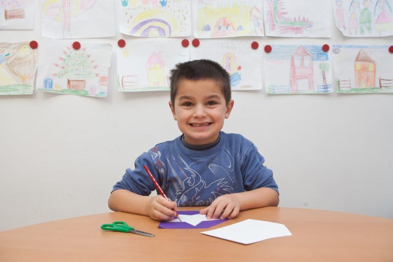 Muhamed zeichnet die Sternform der weißen Vorlage auf das bunte Papier und schneidet den Stern aus.