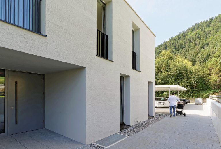 Der Hanglage wegen wird die Wohnanlage in der mittleren Etage betreten. Der Eingang liegt geschützt in die Architektur zurückversetzt. Auf eine Tiefgarage wurde ganz bewusst zugunsten von Carports bzw. freien Abstellplätzen verzichtet.