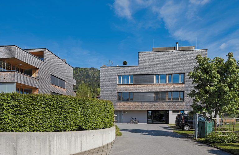 Geschindelte Sachlichkeit Über einem Sockel aus Beton sitzen die beiden Häuser streng konturiert im sanft abfallenden Gelände. Die obersten Etagen wurden als Terrassenwohnungen ausgeführt.