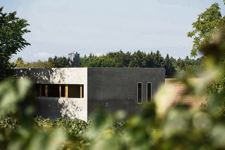 Alurahmen haben die schmalen hohen Fensterschlitze, Rahmen aus Holz die Fensterbänder. Die auf dem flachen, bekiesten Dach liegenden Photovoltaikelemente liefern Strom für die Warmwasserbereitung.
