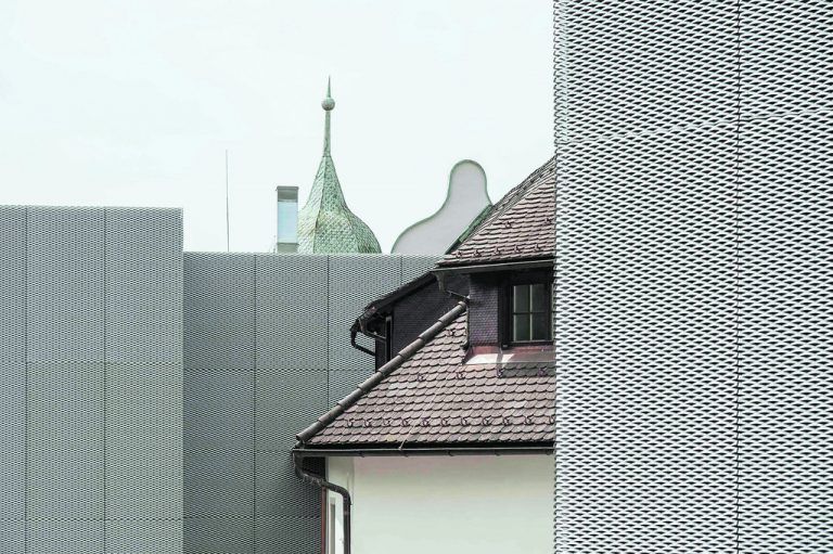 An das Schloss seit- bzw. rückwärts angedockt wurden zwei teilweise in die Erde hineingegrabene Erschließungsbauten, die zur Gänze mit zart perforiertem Alu-Streckmetall ummantelt sind.