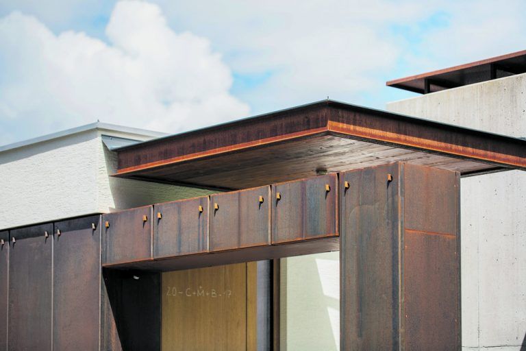 An der Wind und Wetter ausgesetzten Westfassade hat Sebastian Brandner eine Stahlwand aufgehängt, die sehr zur Freude des Architekten bereits malerisch zu rosten beginnt. In sie sind als einzige Öffnungen die Eingangstür und das Garagentor geschnitten.