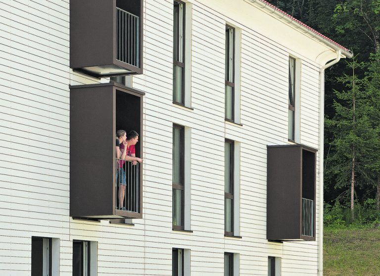 Die braunen Balkone und Fensterrahmen bilden einen reizvollen Kontrast zur weißen Lasierung der aus Holz-Fertigteilen gebauten und perfekt gedämmten Fassaden der zwei RIVA-Gebäude.
