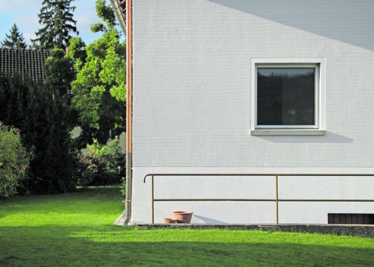 Die Fenster sitzen wieder in Laibungen und werden von glattem Putz gerahmt, glatt sind auch der Sockel und die Außenwand des Stiegenhauses. Die Flächen ringsum haben eine stärker strukturierte Oberfläche.