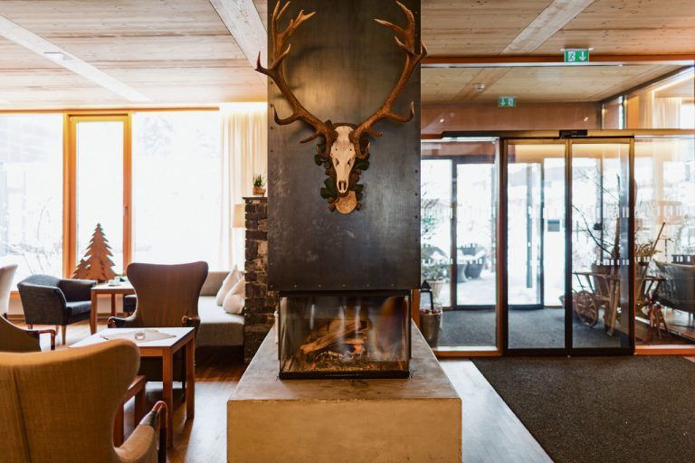 Die Lobby für die Hotel-gäste öffnet sich zum Außenbereich durch eine fast raumhohe Verglasung. Ein offener Kamin sorgt für angenehme Wohnzimmeratmosphäre.