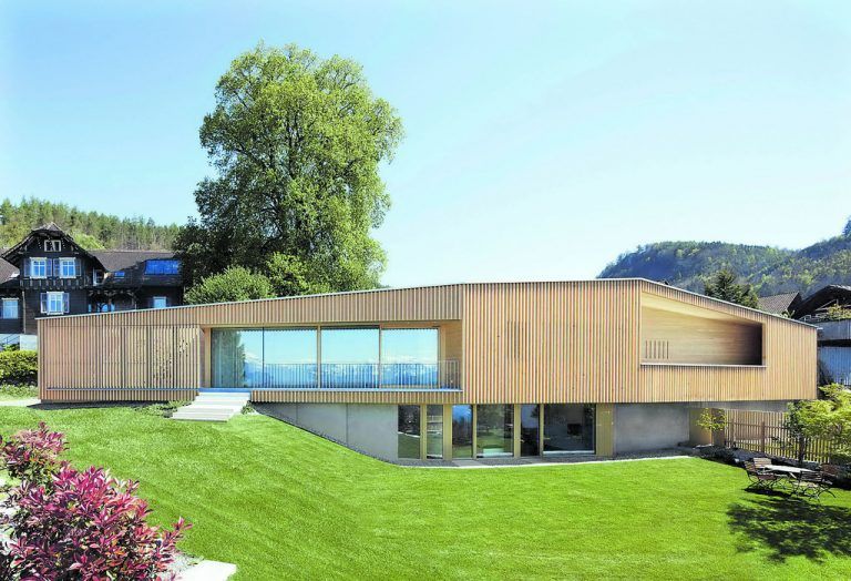 Die obere Wohnebene ist an den schon vorhanden gewesenen Carport angebaut. Tiefe Lamellen aus Weißtanne umhüllen das Ganze, vom Hof, wo sie zu öffnen sind, bis zum Carport. Im Sockelgeschoß aus Sichtbeton ist eine Einliegerwohnung, die zur Zeit noch von der Familie genutzt wird.