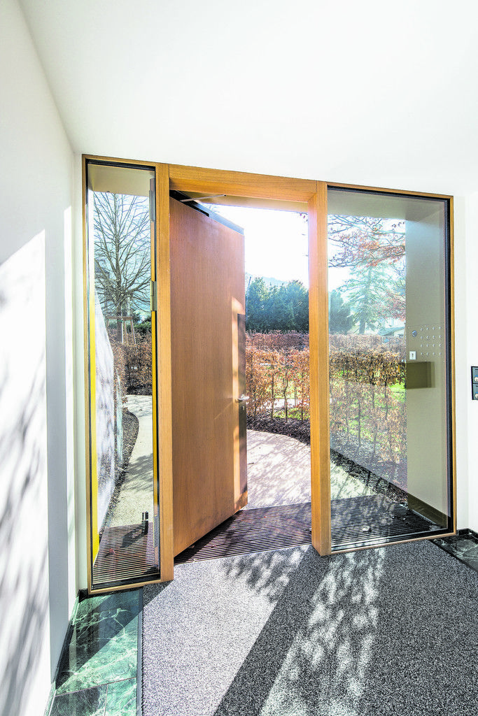 Die Schleuse zwischen innen und außen ist fast unscheinbar. Die Eingangstüren sind wie alle Fenster aus Holz, beidseitig flankiert von verglasten Flügeln.