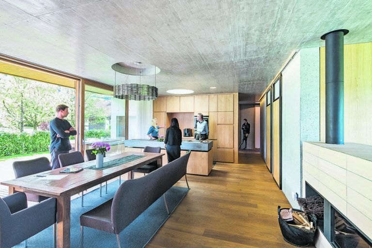Durch raumhohe (Holz-)Fenster, die sich im großen offenen Wohnbereich in einer in den Baukörper hineingezogenen Terrasse fortsetzen, verfilzen Außen- und Innenraum. Die Decke ist aus Sicht-beton, die Böden genauso wie die Türen sind aus geölter Eiche.