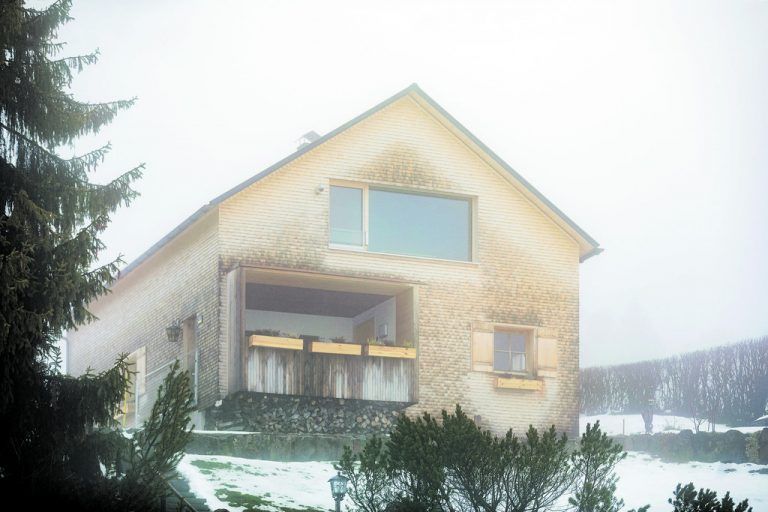Gleich nach der Haustür kommt erst einmal eine Loggia, die durch einen extra Rahmen vor Regen und Schnee geschützt ist. Gegenüber dem Ausblick ins Freie gibt ein großes Fenster Einblick in die Stube.