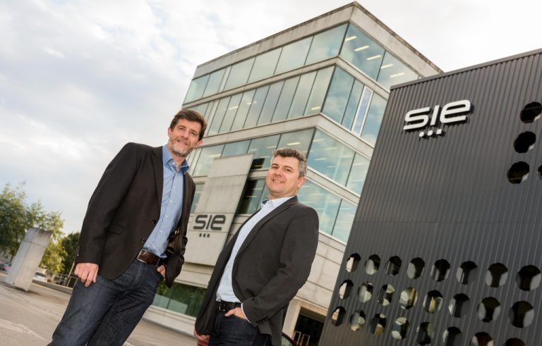 Jürgen Duelli (l.) und Markus Dillinger vor dem S.I.E-Headquarter in Lustenau. Das neue Gebäude (rechts im Bild) ist von einer auffallenden Metallfassade geprägt und beheimatet die Produktion. VN/Stiplovsek