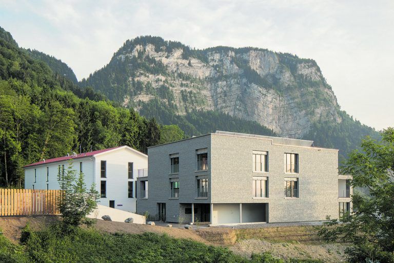 Leistbarer Stufen-Mietkauf in einem aus Holz-Fertigteilen gebauten weißen Haus mit extravagant geschwungenem Giebeldach contra frei finanziertem, massiv gemauer-tem und hölzern verschindeltem Wohnbau mit Flachdach.