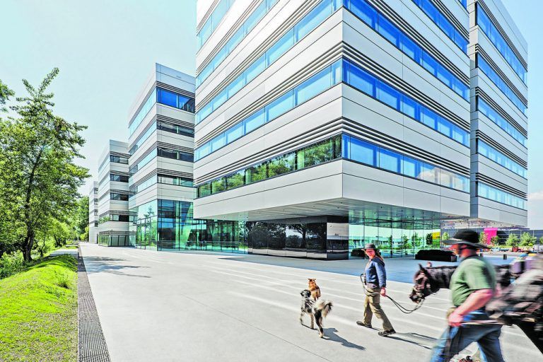 Man betritt den Neubau unter der reflektierenden Untersicht der beiden ersten Bürohochhäuser im rundum verglasten Foyer.