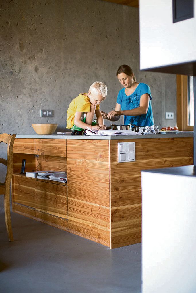 Till hilft seiner Mutter Heike beim Kochen am hölzernen Küchenblock. Die Wand dahinter ist aus Sichtbeton und der Estrich ist hier wie im gesamten Erdgeschoß mit Zement beschichtet.