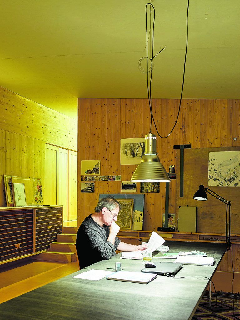 Der Bauherr und Architekt Werner Binotto beim abendlichen Aktenstudium am multifunktionalen Tisch im hohen Hauptraum.