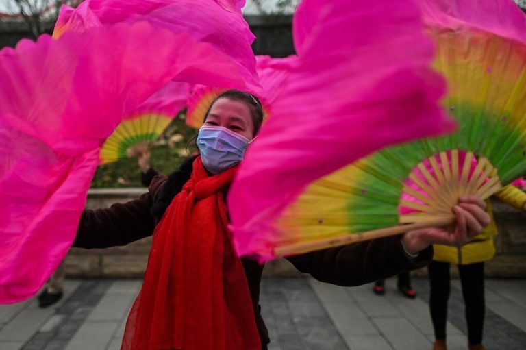 Eine farbenprächtig geschmückte Frau mit Gesichtsmaske gegen Covid tanzt in  der chinesischen Provinz Hubei auf einer Straße in Wuhan. AFP