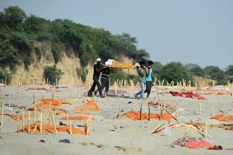 Menschen tragen am Ufer des Ganges eine Leiche an Gräbern vorbei, die mit Safrankleidern von Coronaopfern bedeckt sind. AFP
