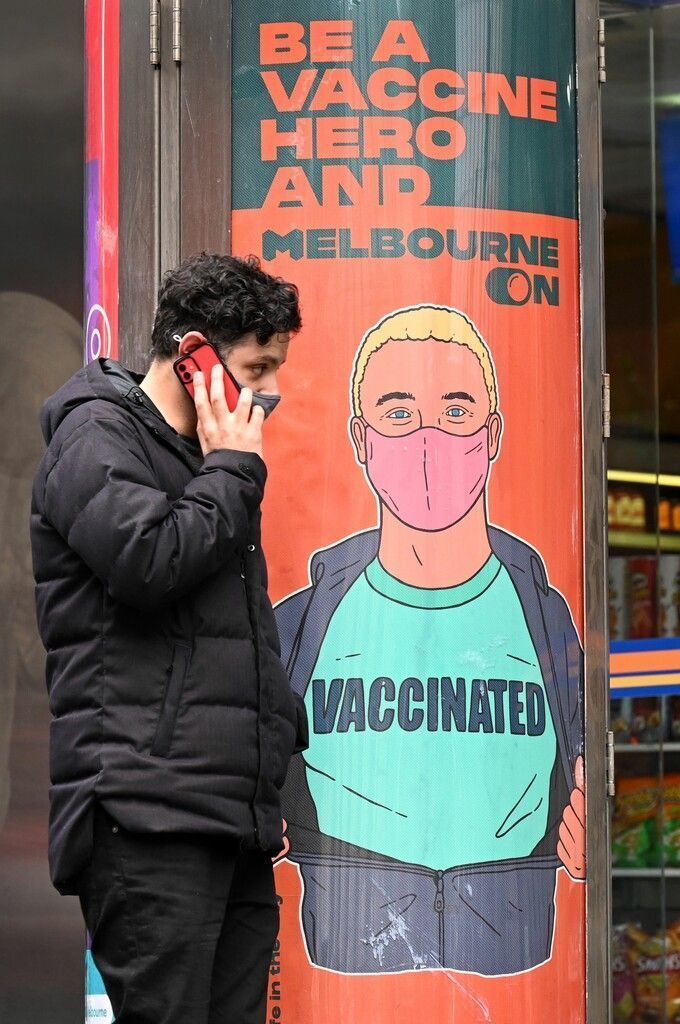 Im australischen Melbourne telefoniert ein Passant neben einem Poster, auf dem für Corona-Impfungen geworben wird. AFP