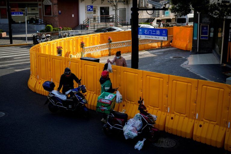 Ein Auslieferer reicht einer Frau Essen über eine Absperrung in Schanghai, China. Das Viertel befindet sich im Lockdown. Reuters