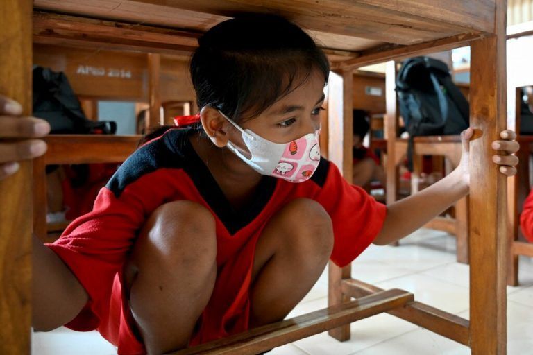 Bei einer Erdbeben- und Tsunami-Übung auf Bali nimmt ein Kind eine Schutzposition unter einem Tisch ein. AFP