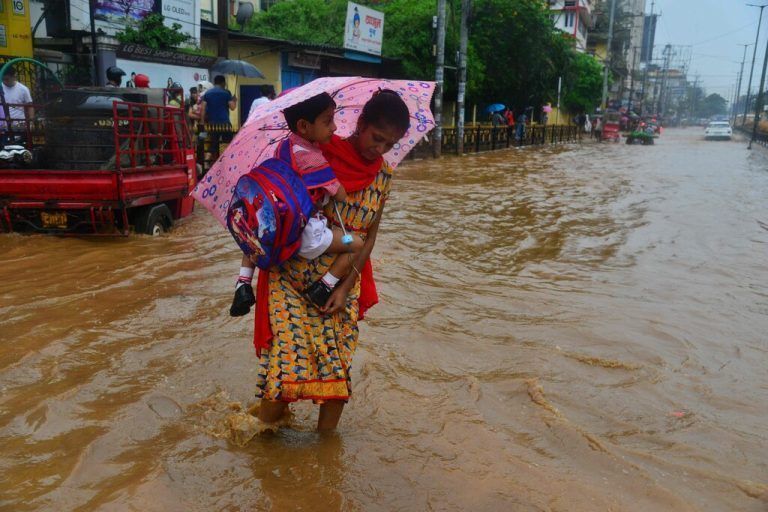 Über eine überflutete Straße in der Stadt Guwahati im indischen Bundesstaat Assam trägt eine Frau ihren Sohn. AFP