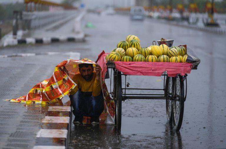 Um sich vor einem plötzlichen Regenguss zu schützen, bedeckt sich ein Obstverkäufer in Jammu, Indien, mit einer Plastikplane. AP