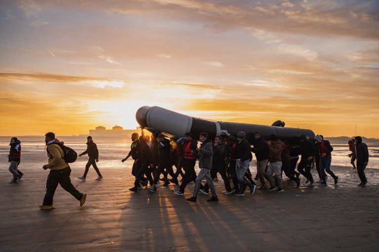 Migranten tragen ein Schlauchboot auf ihren Schultern, als sie sich darauf vorbereiten, am Strand von Gravelines in der Nähe von Dünkirchen den Ärmelkanal Richtung Großbritannien zu überqueren. AFP
