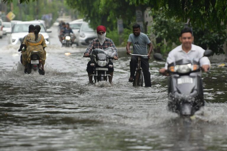 Nach einem heftigen Regenschauer in der indischen Stadt Amritsar bahnen sich Pendler ihren Weg durch eine überflutete Straße. AFP