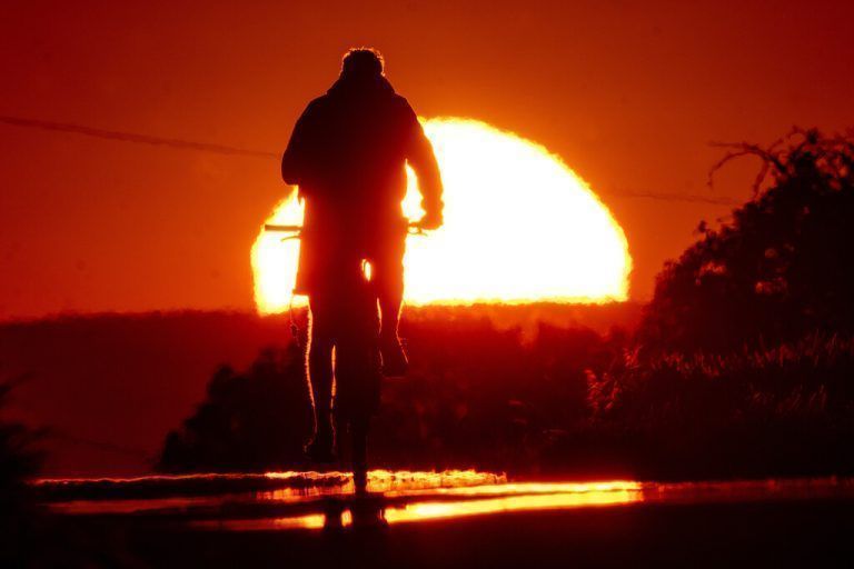 Während des Sonnenaufgangs fährt ein Mann mit seinem Fahrrad eine Straße am Stadtrand von Frankfurt entlang. AP