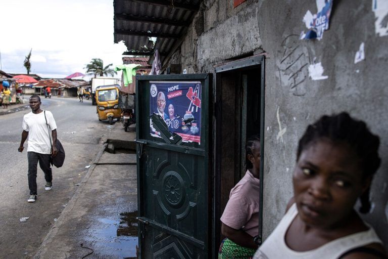Eine Passantin steht in Monrovia neben einem Plakat von Präsident George Weah. Die Wahlen in Liberia finden am 10. Oktober statt. AFP