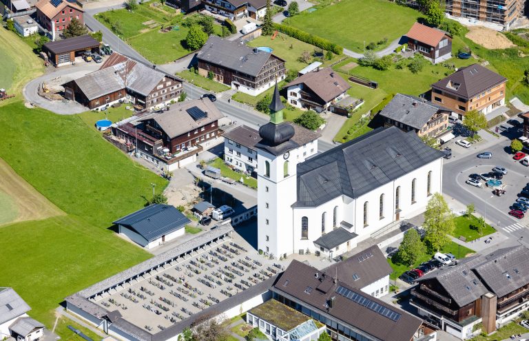 Luftbild der Pfarrkirche Hl. Drei Könige und Arkadenfriedhof mit umliegenden Häusern. <span class="copyright">Volare</span>