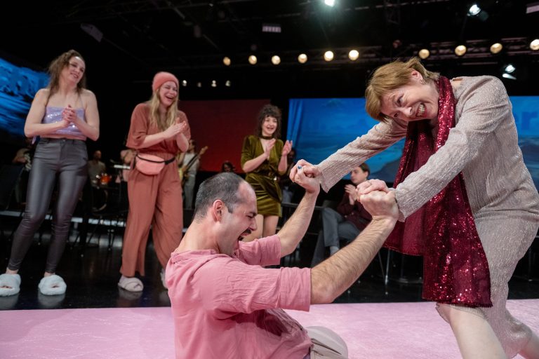 Auf einem bleichen lachsrosa-farbenen Catwalk werden die Zuschauer quer über die Bühne zu ihren Sitzmöglichkeiten geleitet.