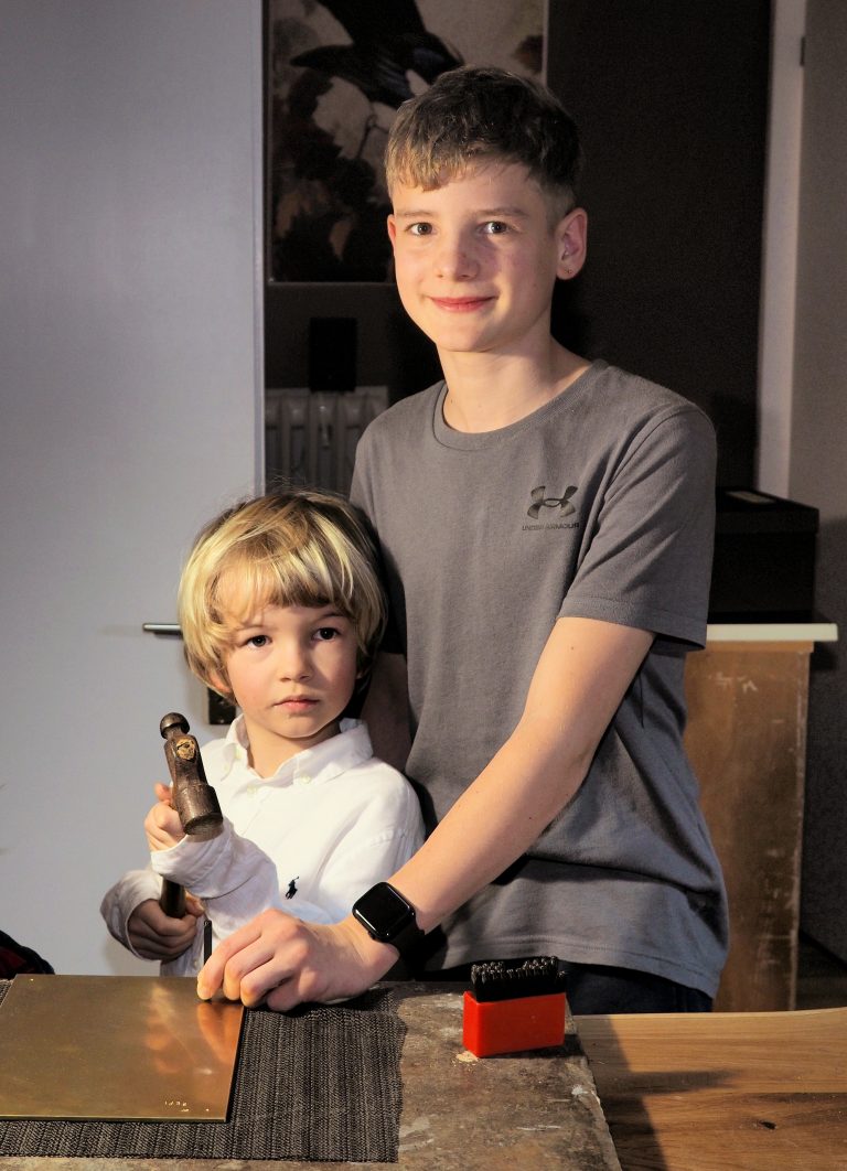 Nias und Jakob prägen ihre Namen auf eine Messingplatte.