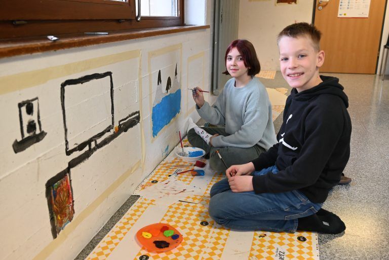 Rosalie und Anton haben es sich an der Wand vor ihrer Klasse gemütlich gemacht. - Schüler bemalen ihre Schule - Schüler bemalen ihre Schule