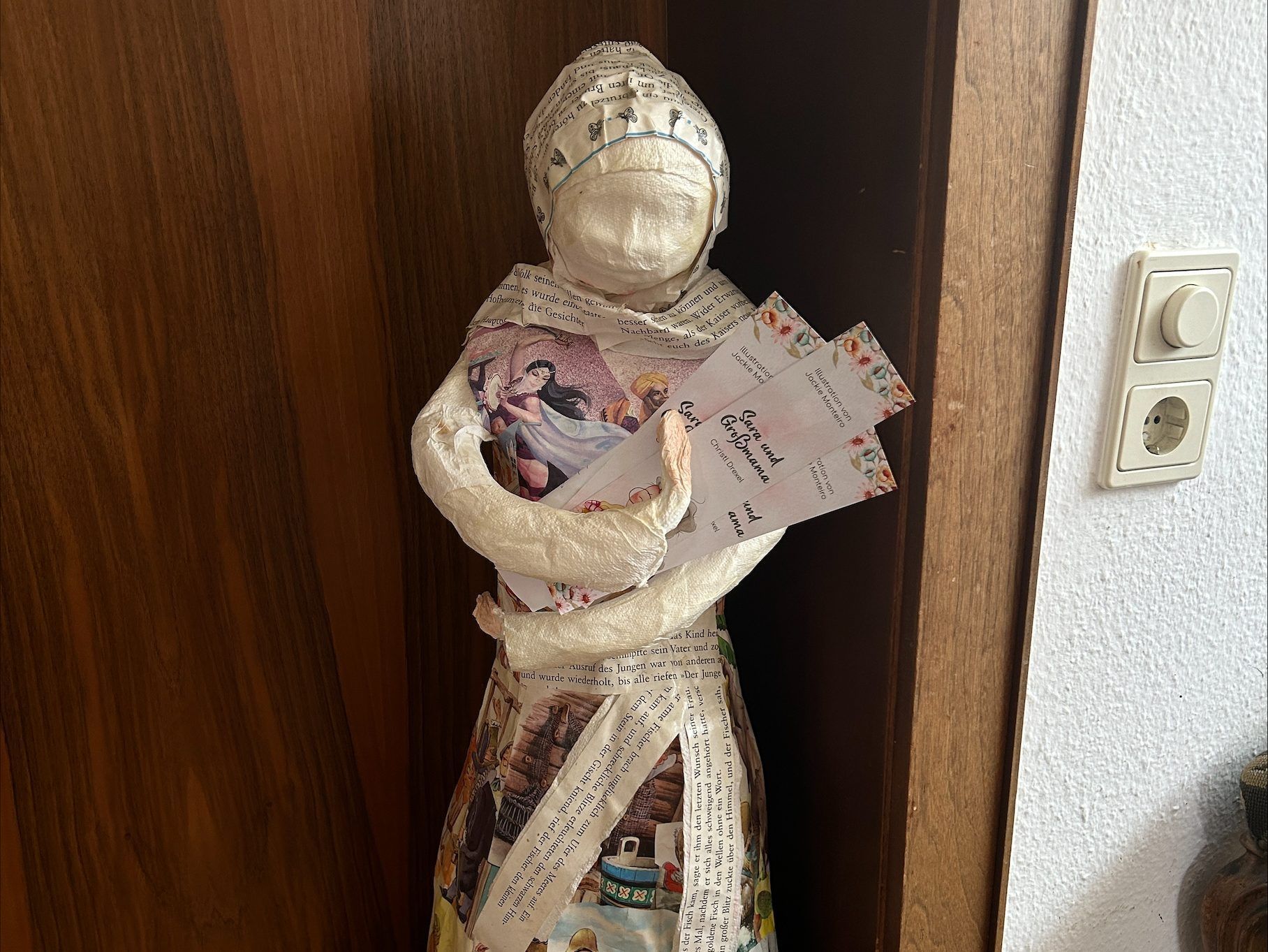 Diese Skulptur hat Christl selbst gemacht, sie hält Flyer des Buches in der Hand.