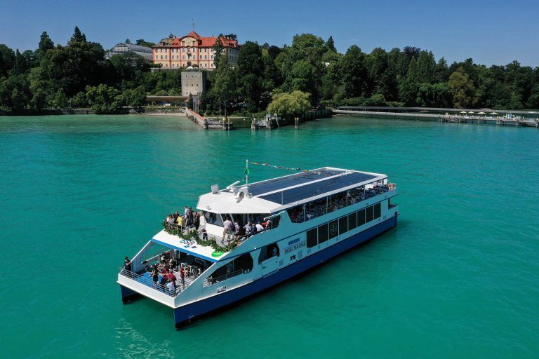 ARCHIV - 17.07.2022, Baden-Württemberg, Insel Mainau Im Bodensee: Der neue batteriebetriebene E-Katamaran "Insel Mainau" fährt nach der Taufe im Juli vom Landesteg vor der Insel Mainau über den Bodensee Richtung Unteruhldingen (Aufnahme mit einer Drohne