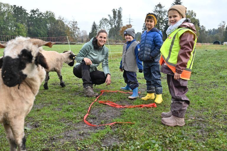 Inmitten der Schafe und Ziegen legen die Kinder ein "E" auf den Boden. Klassenvorstand Nina Schlattinger hilft ihnen dabei. - Mit Tieren und an frischer Luft lernt‘s sich leichter - Mit Tieren und an frischer Luft lernt‘s sich leichter