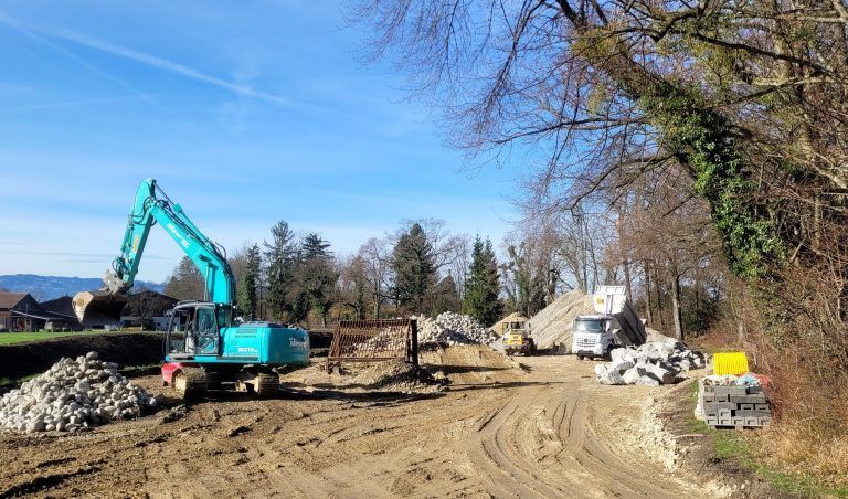 BU 6 UMSCHLAGPLATZ: Die Großbaustelle am Ruggbach mit dem „Umschlagplatz“ zur Zwischenlagerung der Baumaterialien samt dem Mutterbodendamm auf Lochauer Seite. - Hochwasserschutzprojekt Ruggbach: Erneuerung der Brücke L190 - Hochwasserschutzprojekt Ruggbach: Erneuerung der Brücke L190