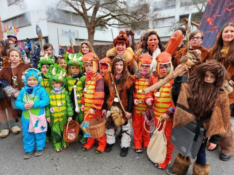 Ore-Ore-Kinderfasching mit großartigem Umzug in Lochau: Im neuen Outfit präsentierten sich die „Berger Steinzeitmenschen“ mit dem Lochauer Faschingsbürgermeister Roman Rist zusammen mit neuem Umzugswagen und Faschingssong, mit Keulen und Speeren sowie den kleinen Dinos beim Lochauer Umzug.