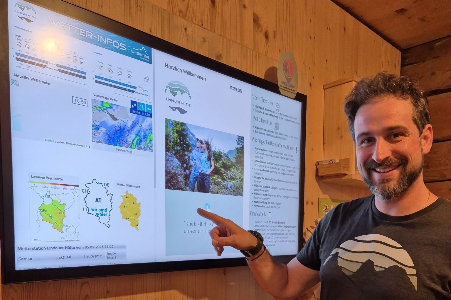 Der technikaffine Hüttenwirt Stefan Köberle präsentiert den Informationsbildschirm, der extra angeschafft wurde. Hier finden die Gäste immer den aktuellen Wetterbericht, Tourenvorschläge und weitere wichtige Informationen zu ihrem Aufenthalt auf der Lindauer Hütte.