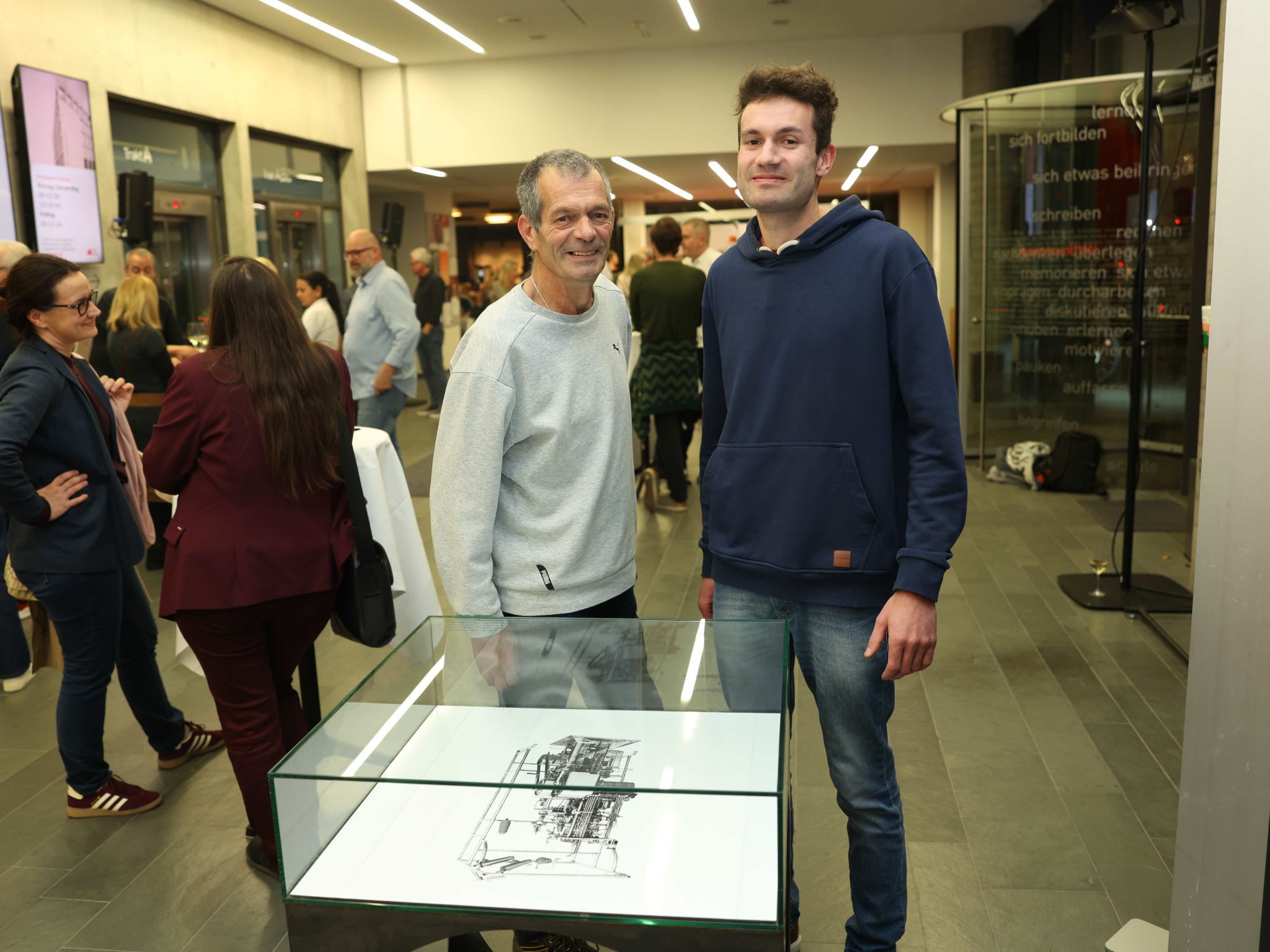 Albrecht und Julian Schwärzler vor dem Bild einer Wirkmaschine.