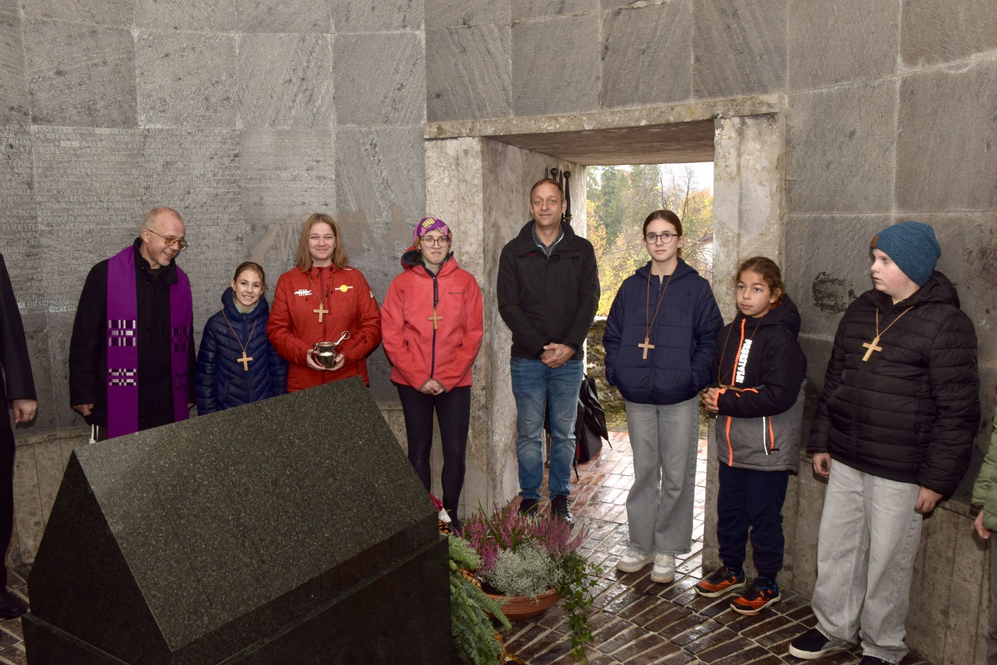 Pater Guido (l.) mit Ministrantinnen, Ministranten und einem Besucher am Allerseelentag in der Krypta des Bludenzer Kriegerdenkmales.