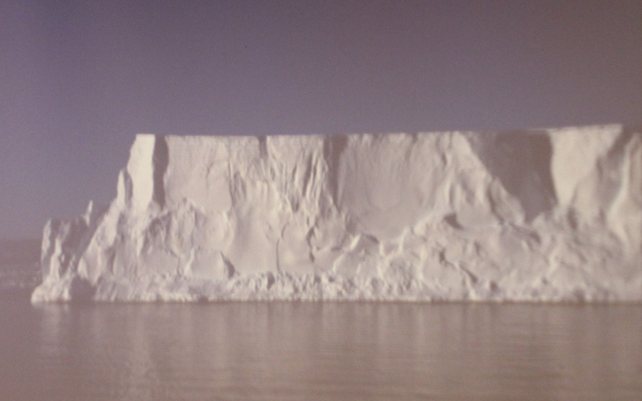 Die Aufnahme zeigt nur einen kleinen Ausschnitt eines riesigen Eisbergs, rund fünf Kilometer lang und über 100 m hoch aus dem Wasser ragend – etwa neun Zehntel des Giganten, der etwa einen Kilometer in die Tiefe reicht, sind unter Wasser.