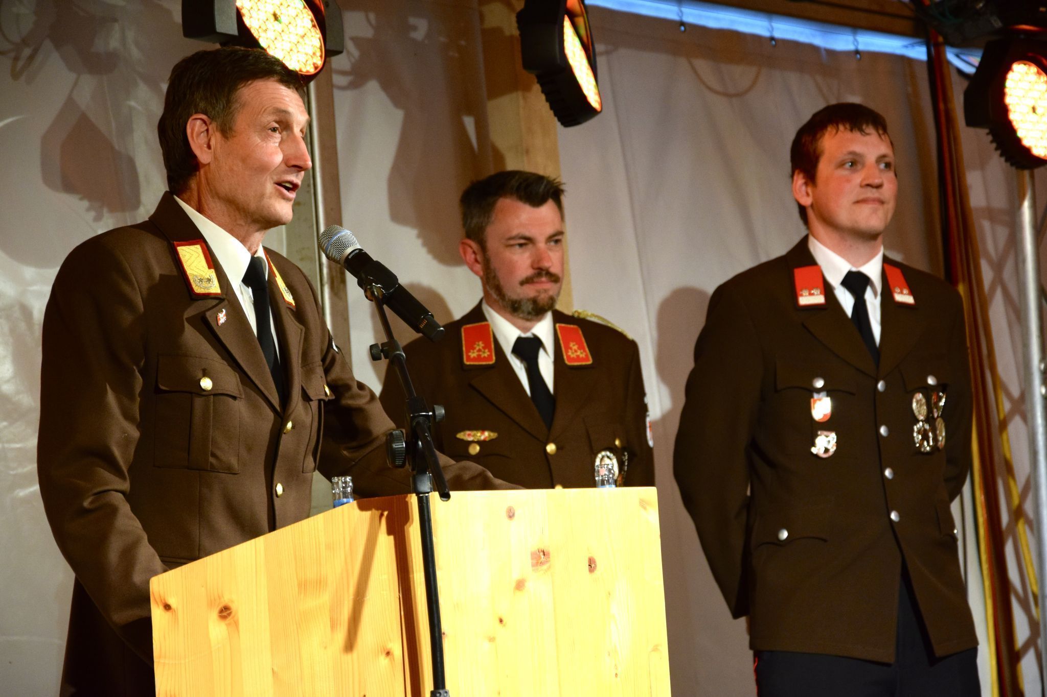 Landesfeuerwehrinspektor Herbert Österle am Rednerpult, neben ihm der Schrunser Feuerwehrkommandant Martin Jenny und der Jugendleiter der Feuerwehrjugend Schruns, Dominique Geiger.