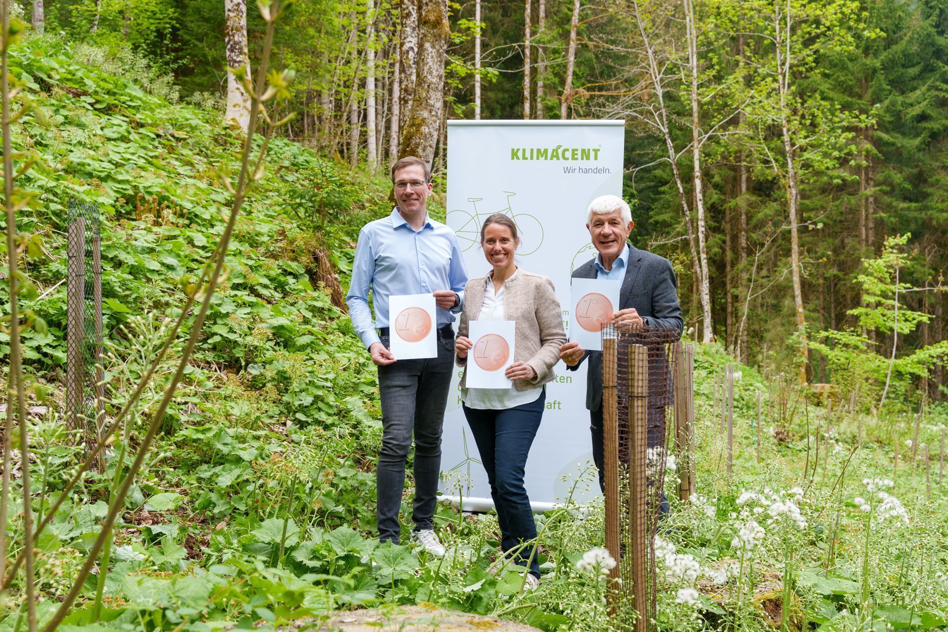 Halten den Klimacent hoch: (v.li) Bgm. Florian Küng, Mag.a FH Cordula Kreidl von der Arge Erneuerbare Energie Vorarlberg und DI Thomas Ölz vom Vorarlberger Waldverein, der als Partnerbetrieb den Klimacent „Wald und Holz“-Fonds über den Waldverein managt.