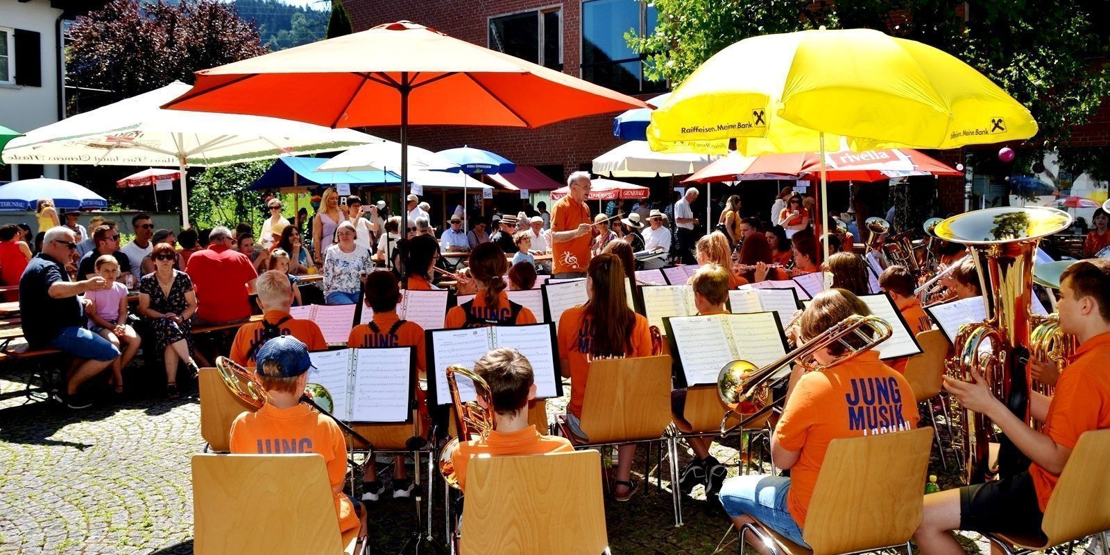 Einladung zum stimmungsvollen „Sommerfest der Pfarre Lochau“ auf dem Platz vor dem Pfarrheim Franz Xaver – ein blasmusikalischer Frühschoppen in geselliger Atmosphäre.