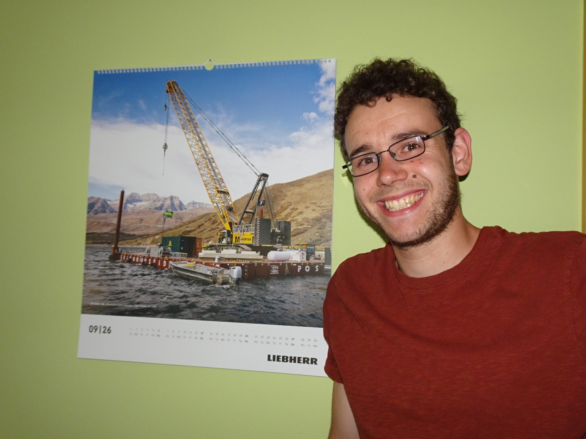 Simon vor einem - natürlich - Kran-Kalender der Firma Liebherr, bei der er seinen Traumjob ausüben darf. 