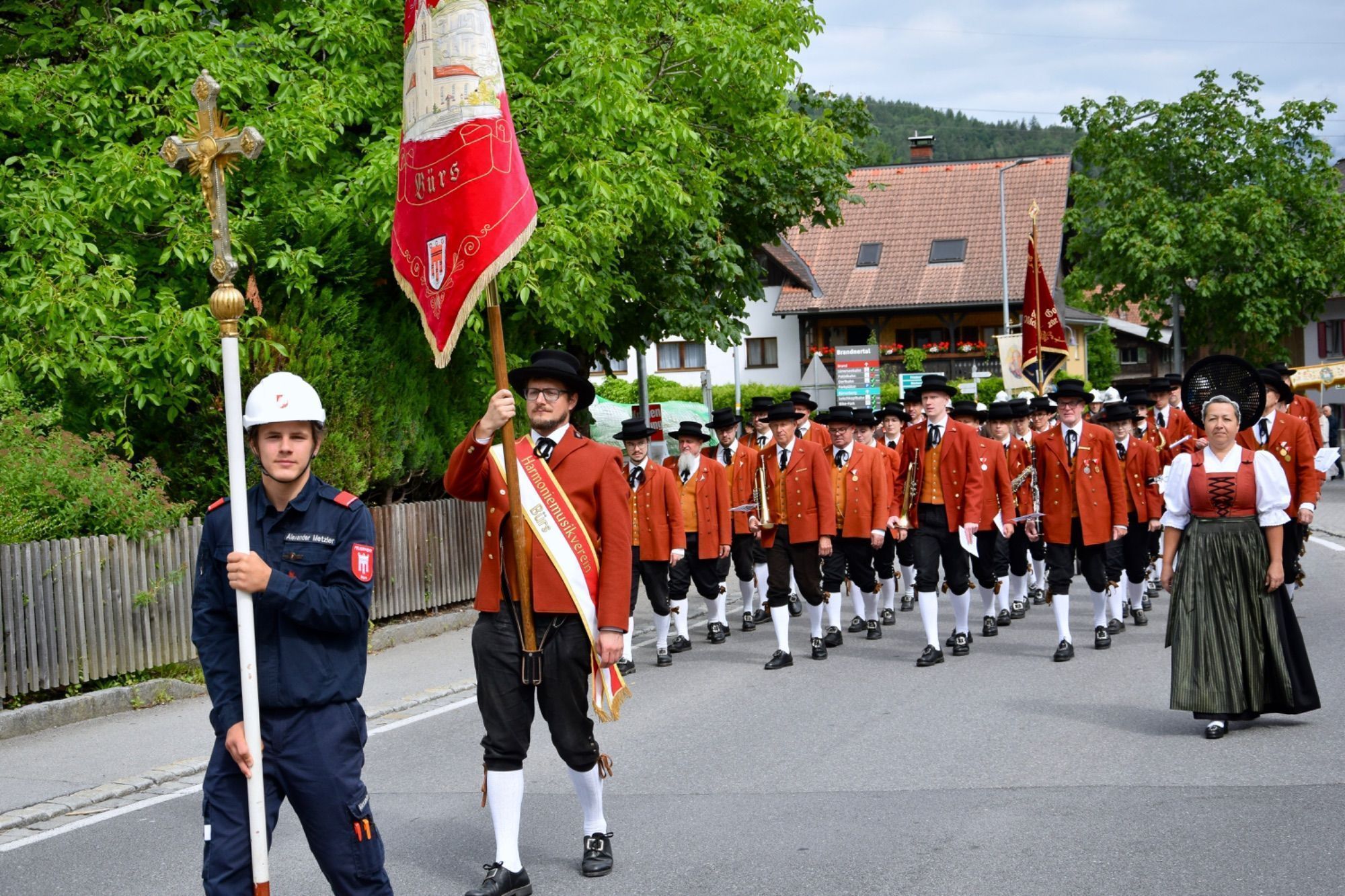 Ein junger Mann der Bürser Feuerwehrjugend trug das Kreuz - dahinter die Harmoniemusik Bürs mit ihrem Fährich und einer Marketenderin.