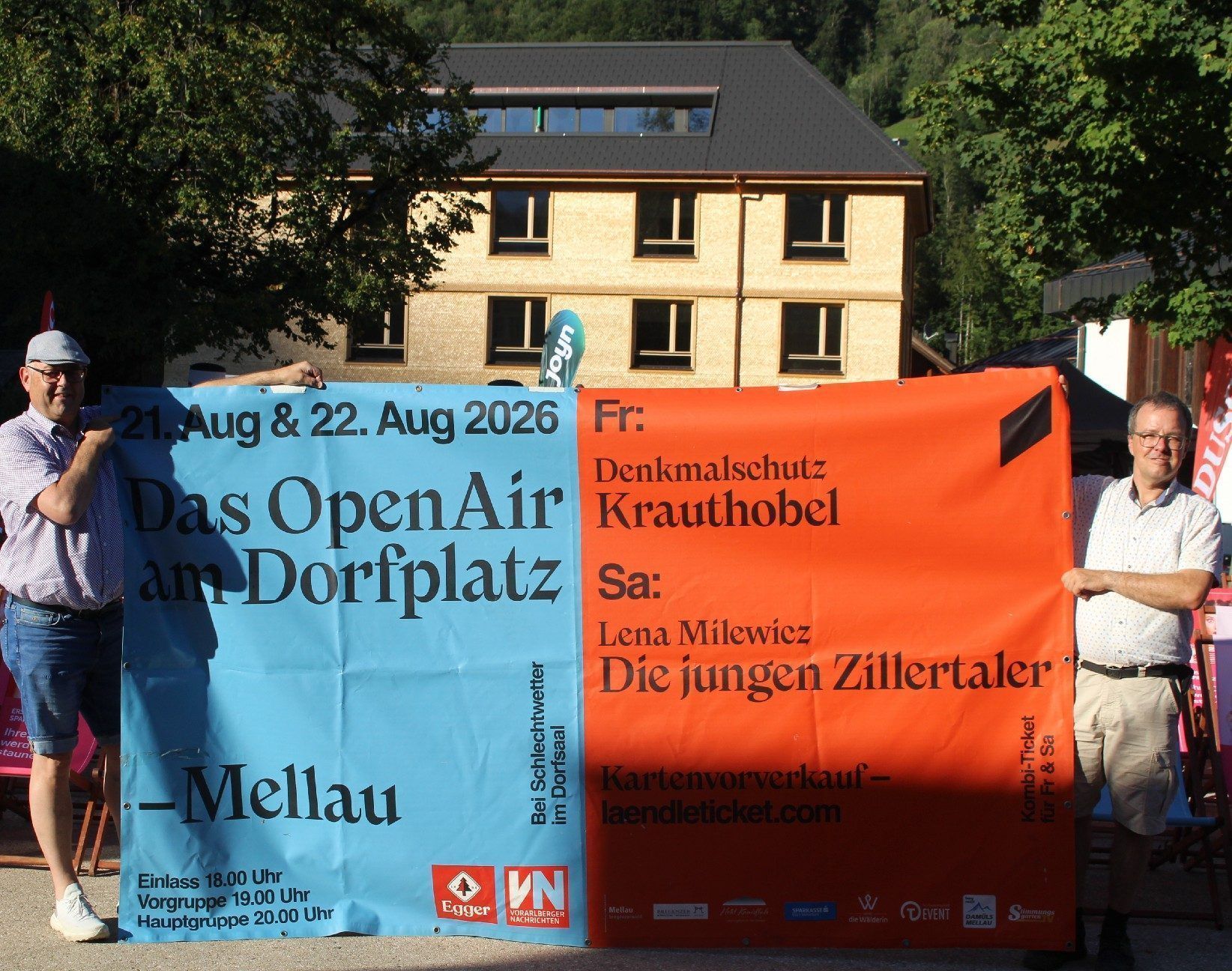 Bürgermeister Tobias Bischofberger (re.) und Alexander Feurstein rühren die Werbetrommel für das Open-air auf dem Mellauer Dorfplatz. Im Hintergrund das im Bau befindliche neue Schmuckstück der Gemeinde. PETER STRAUSS   