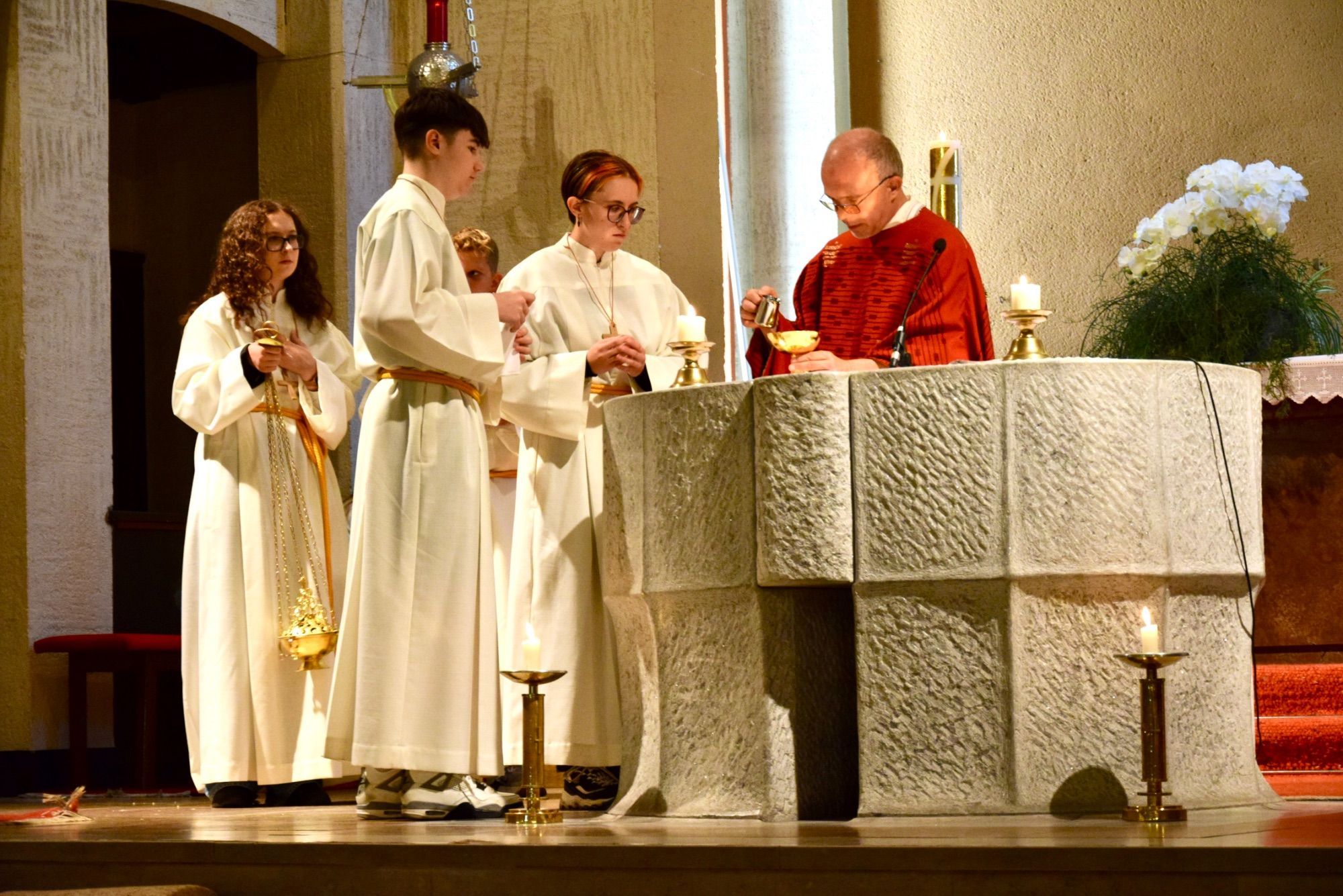 Pater Guido Kobiec mit Ministrantinnen und Ministranten am Altar der Heilig-Kreuz-Kirche Bludenz; geschaffen hat ihn Bildhauer Herbert Albrecht vor genau 50 Jahren, im Jahr 1976.